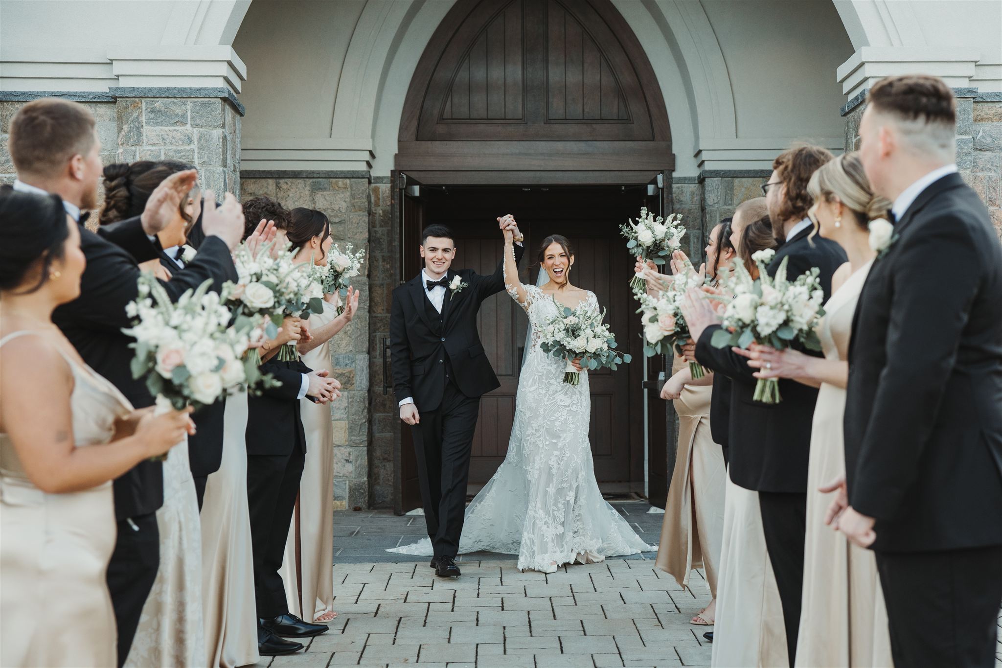 a bride and groom walking out of the aria chapel while the groomsman and bridesmaids cheer