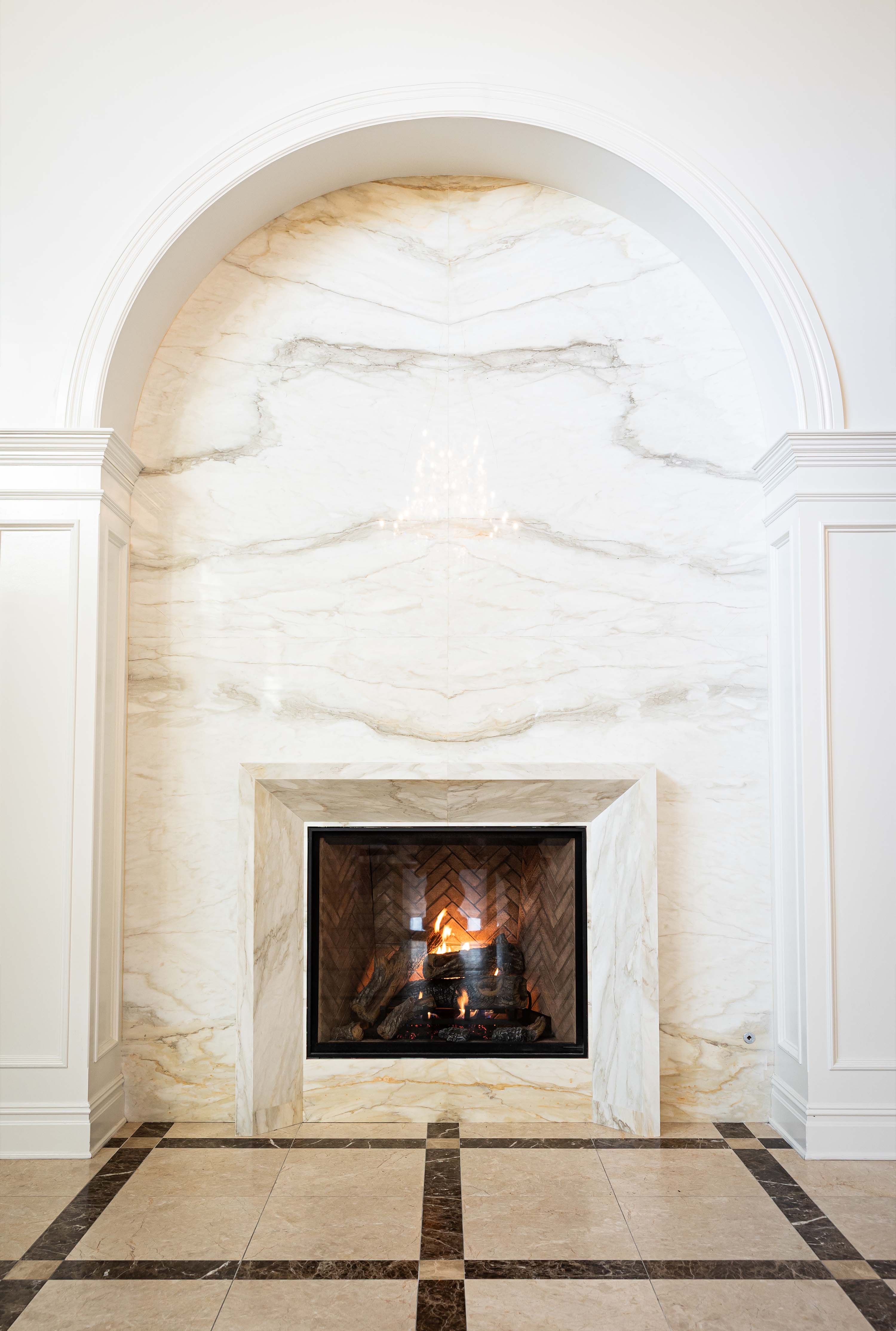 a fireplace accented by a marble wall and an arch