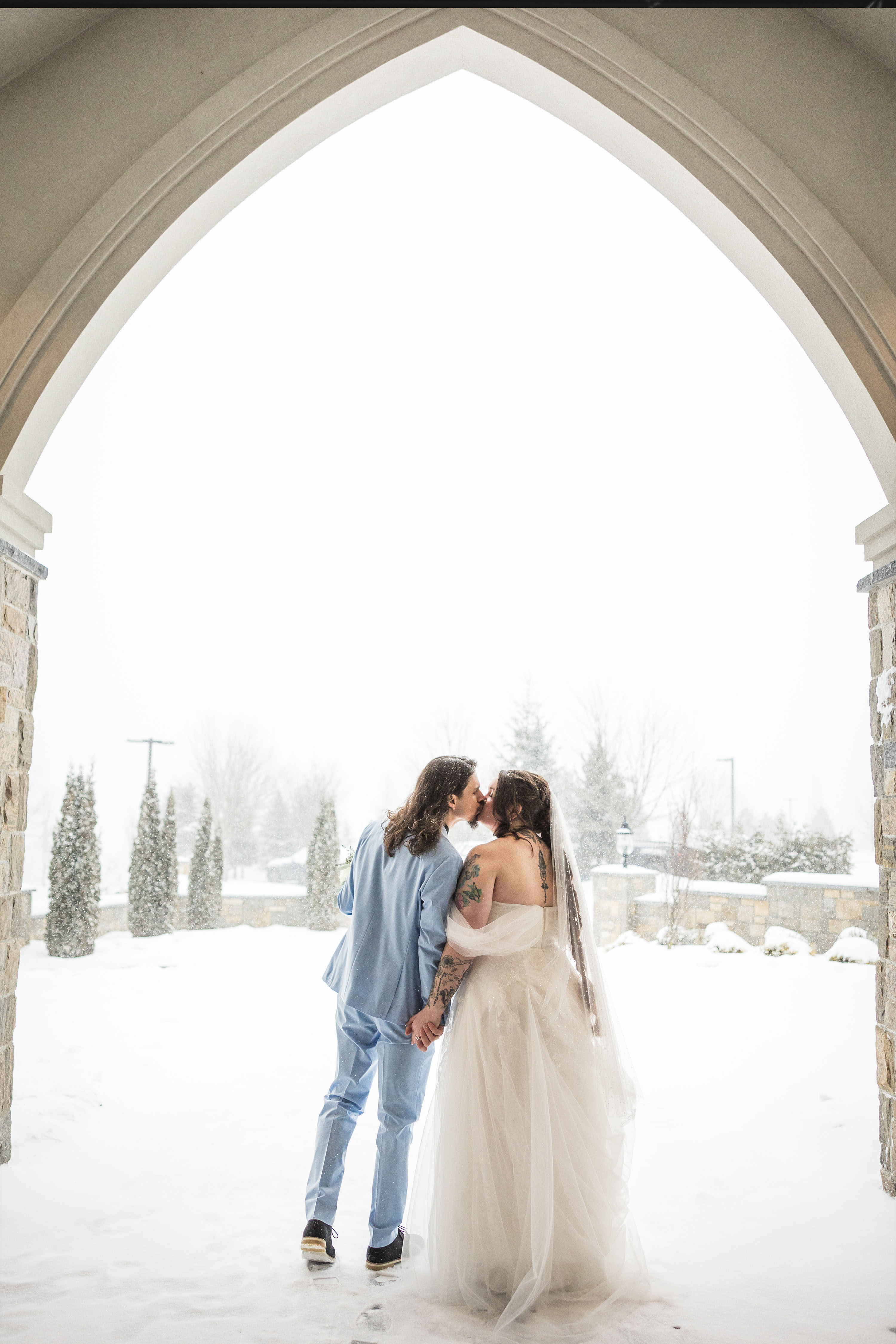 a bride and groom kissing outside the aria chapel in the snow