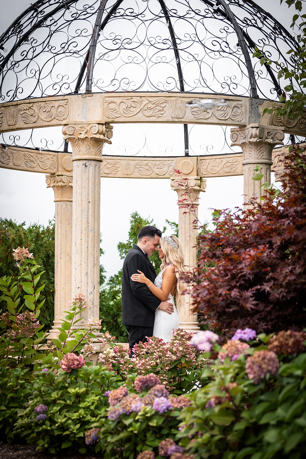 a bride and groom hold each other while standing outside under a gazebo