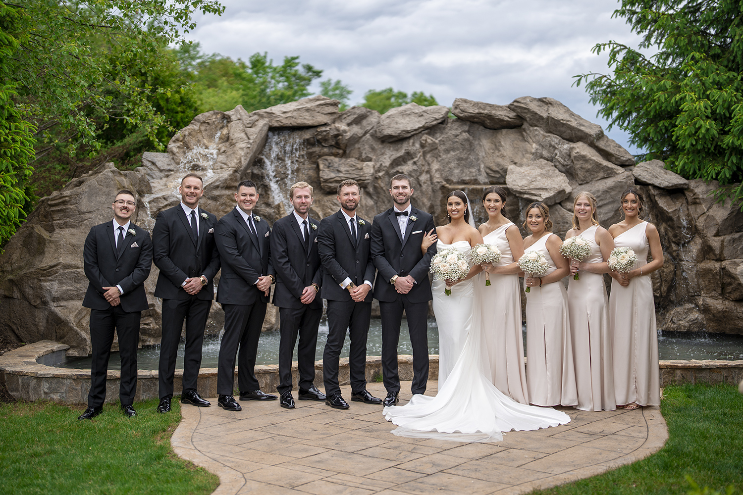 a bride and groom posing outside with their entire wedding party in front of a fountain