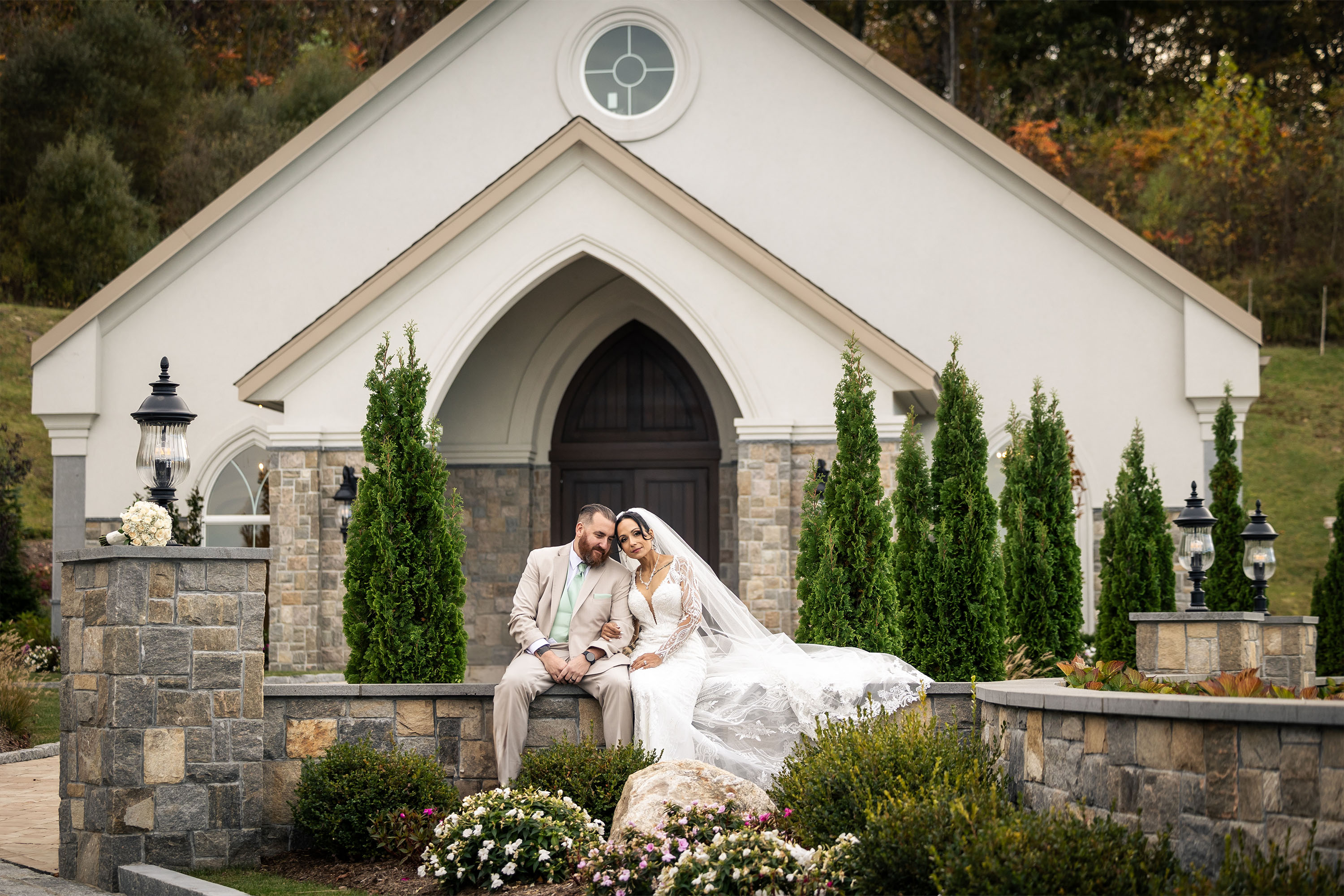 a bride and a groom sitting on a rock wall outside aria chapel