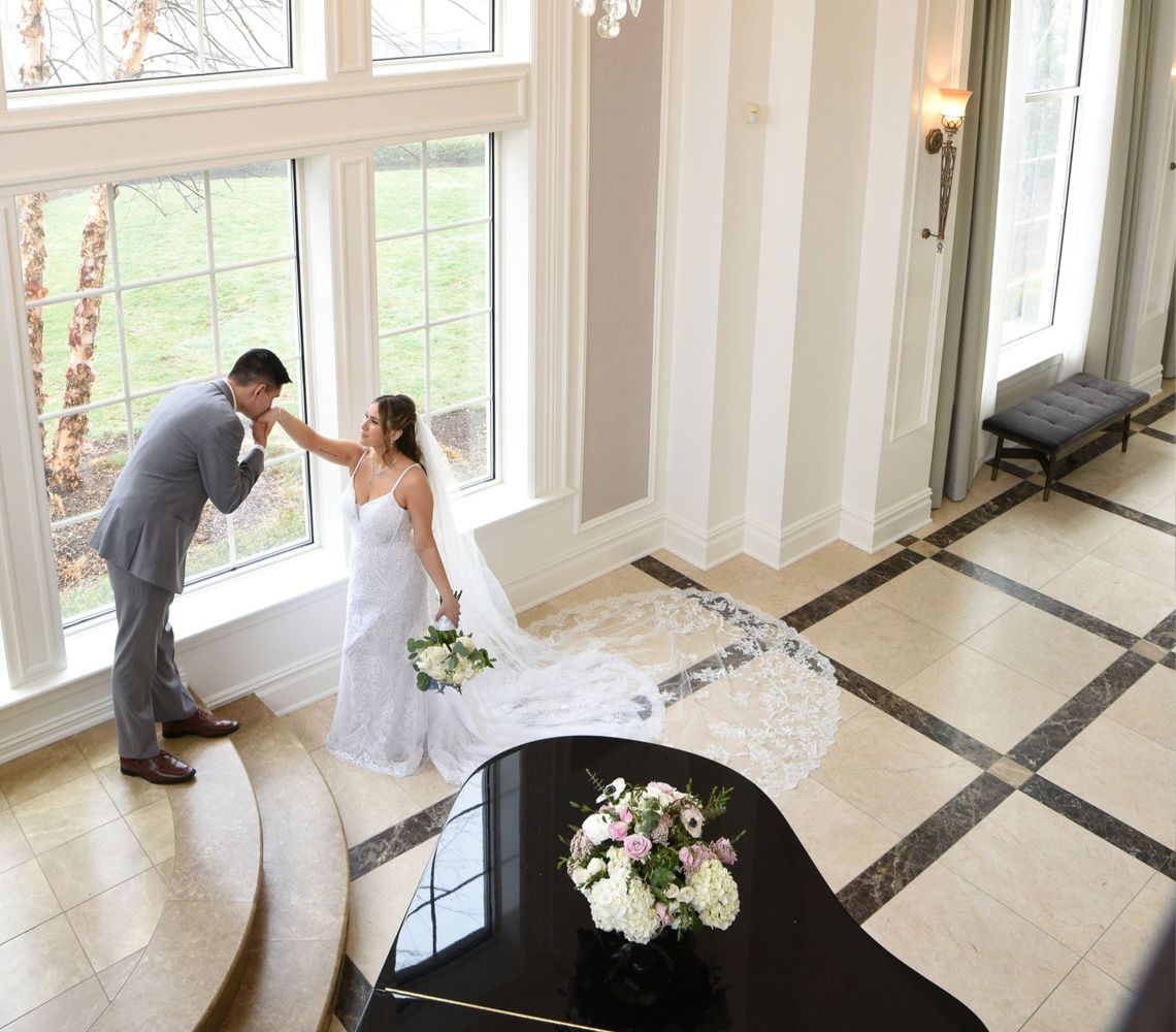 a bride and groom standing a spacious room while the groom kisses the brides hand