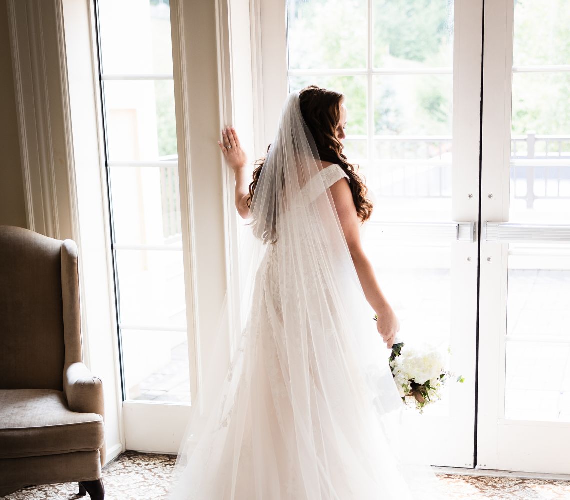 a bride showing her veil standing in front of a window
