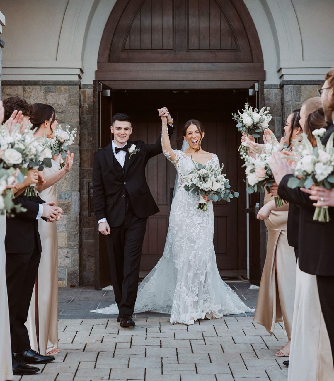 Bride and groom holding hands up in the air with wedding party cheering.