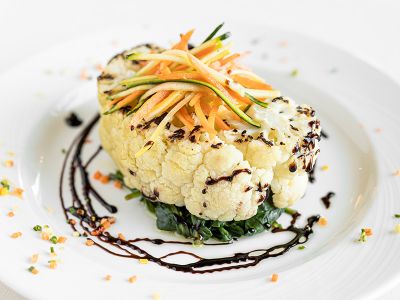 Elegantly plated cauliflower steak with colorful garnish.