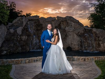a bride and groom posing outside in front of a fountain with a beautiful sunset in the background