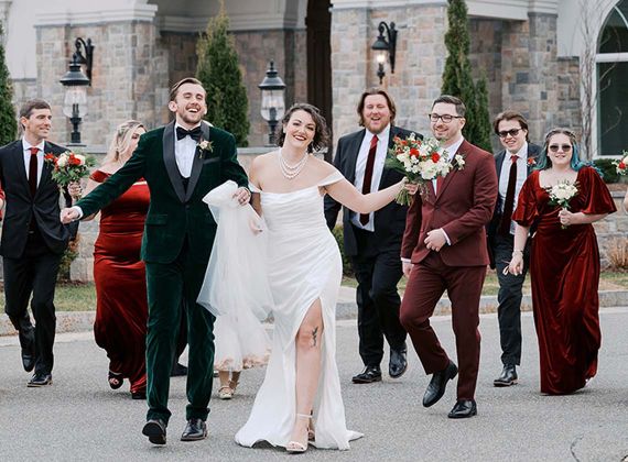 a bride and groom walking outside while the wedding party follows 