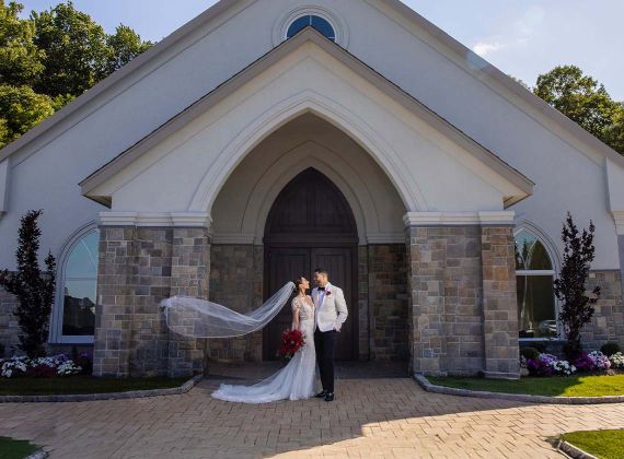 Bride and Groom in front of a chapel with her veil flying in the wind