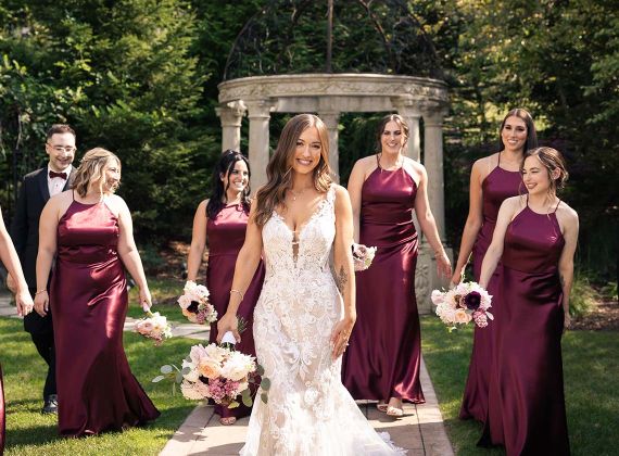 
Bride smiling outside with her bridesmaids and groomsmen behind her in the background